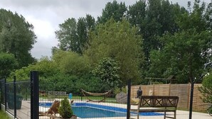 A fenced backyard with a pool, a hammock, and a wooden bench. - La Chaiserie (Romeries)