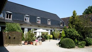 A two-story building with a dark tiled roof, a gravel courtyard, potted plants, and outdoor furniture. - La Ferme Des Buis (Sainghin-en-Weppes)