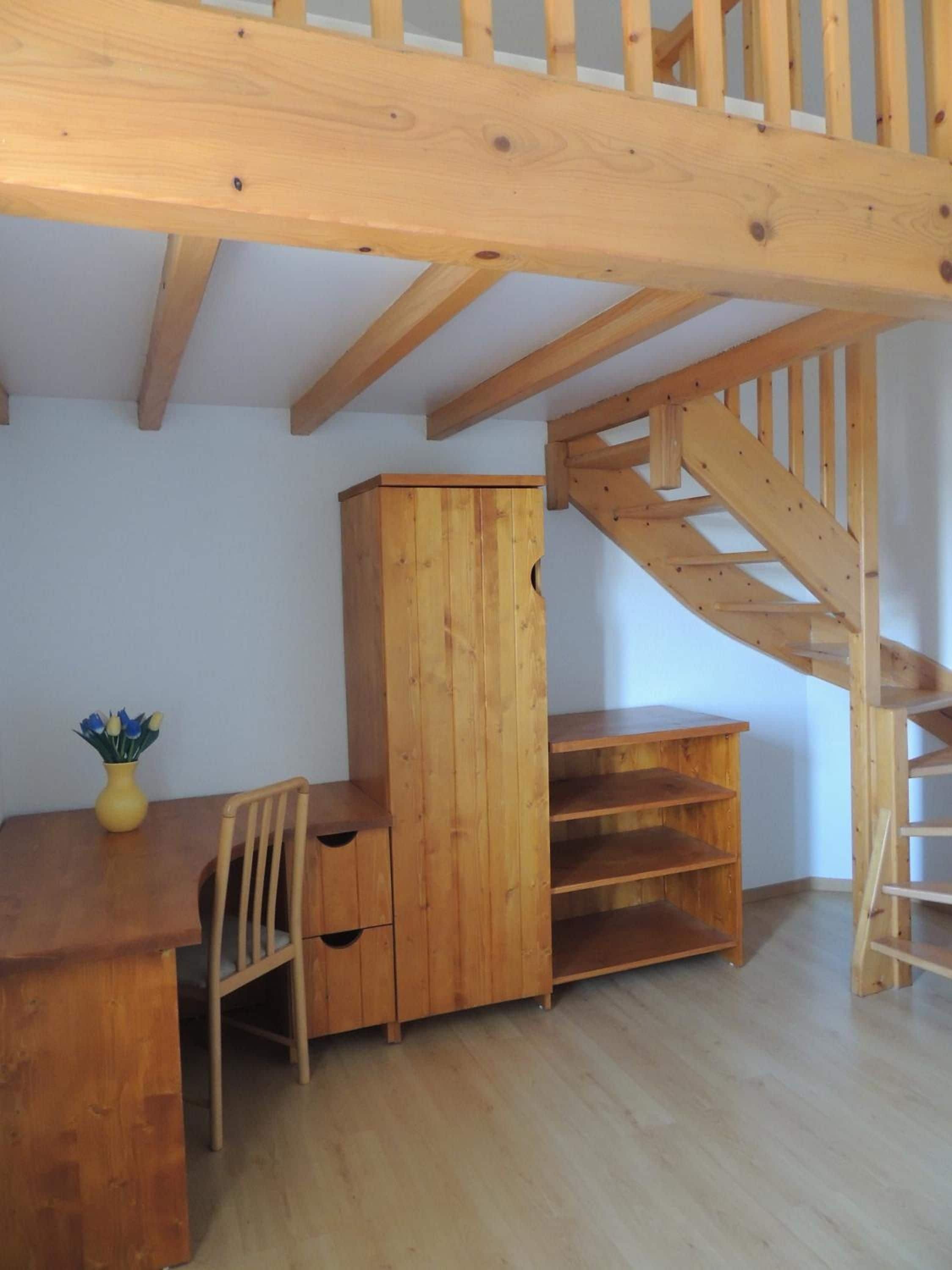 A room with a wooden desk, a chair, a cabinet, and a wooden staircase.