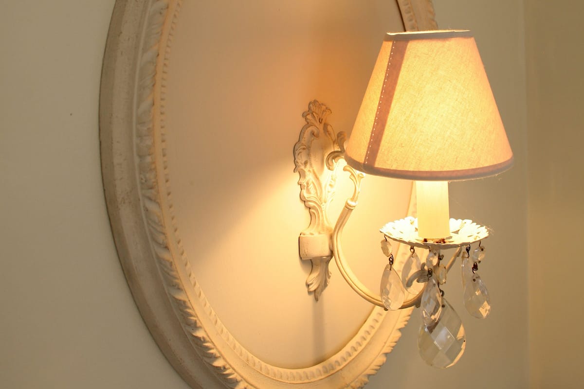 A wall-mounted mirror with an ornate frame and a wall sconce with a lamp.