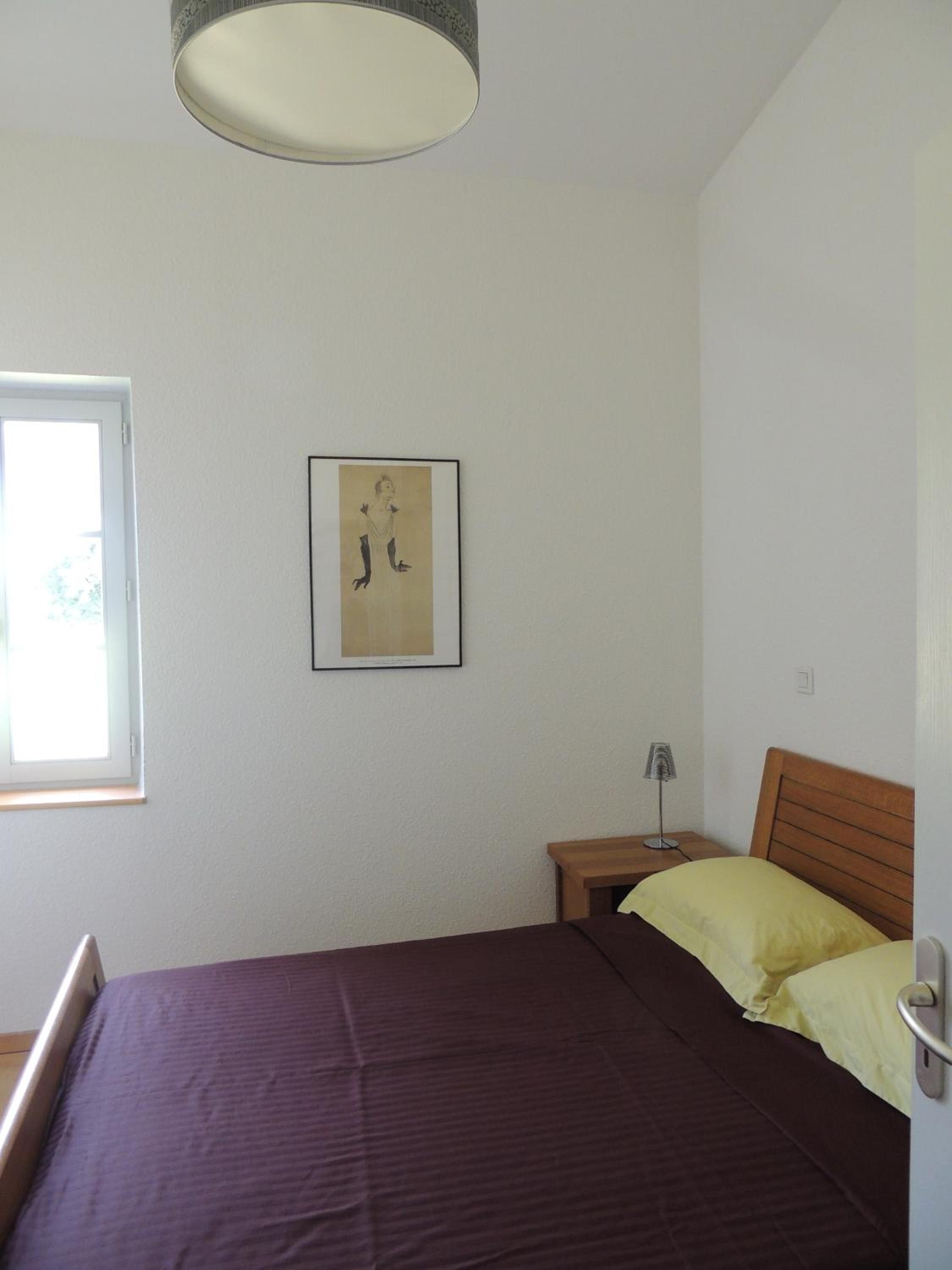 A bedroom with a bed, a bedside table, a lamp, and a window.