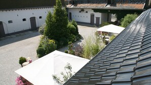 A courtyard with a tiled roof, white walls, and a large tree. - La Ferme Des Buis (Sainghin-en-Weppes)