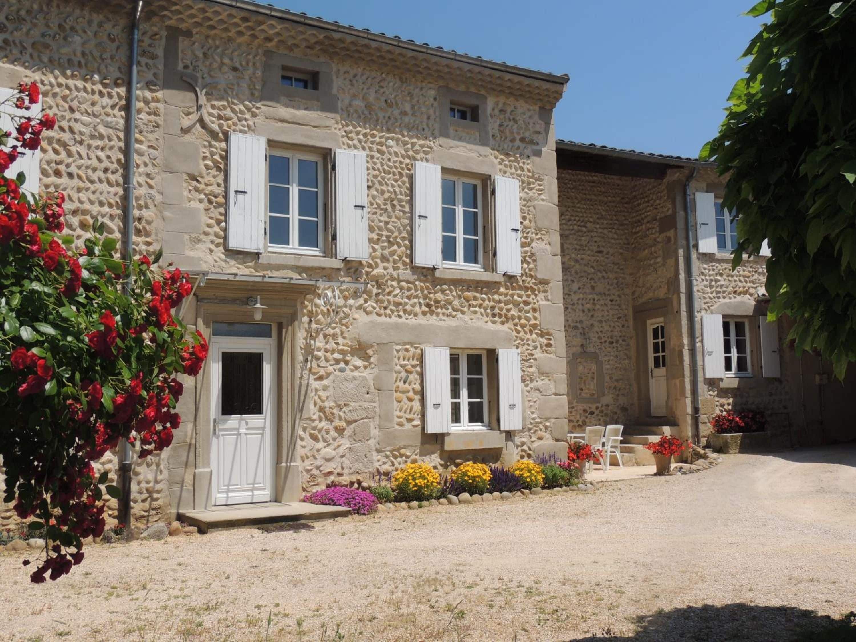 A stone building with white shutters, a door, and a small porch area with flowers.
