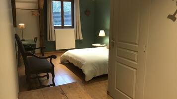 A bedroom with a bed, a chair, a table, a lamp, and a window with curtains.