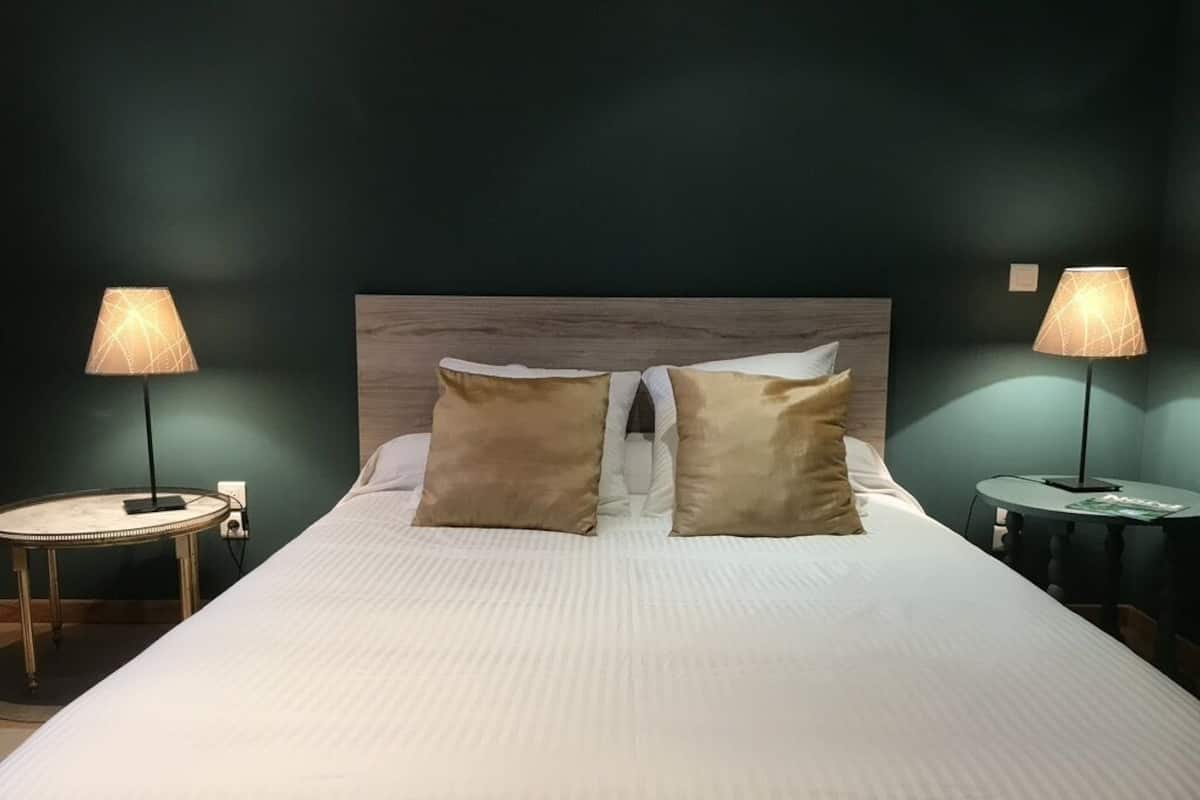 A neatly made bed with two pillows, a round bedside table with a lamp, and a similar table on the opposite side of the bed.