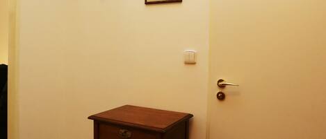 Una habitación con un armario de madera, un perchero, un cuadro enmarco y una puerta blanca.