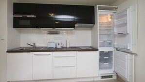 A compact kitchen with white cabinets, a black microwave, a built-in oven, a sink, and a white refrigerator with a freezer compartment. - Greg Apartments Kampa Prague (Prague)