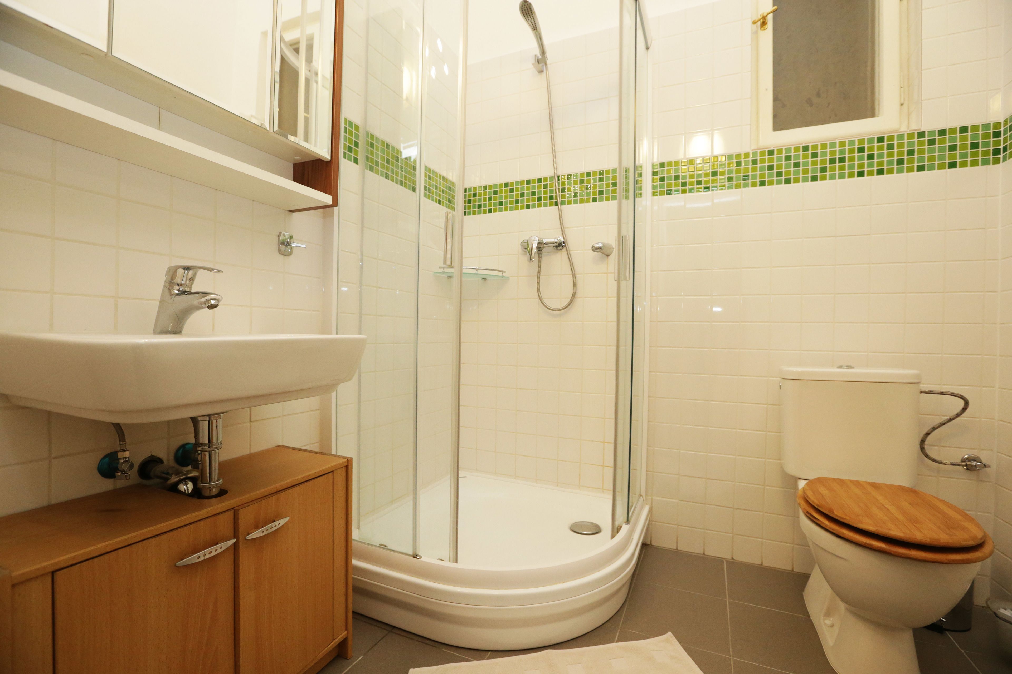 Une salle de bain avec une douche à parois de verre, un meuble-lavabo en bois et des toilettes avec un abattant en bois.