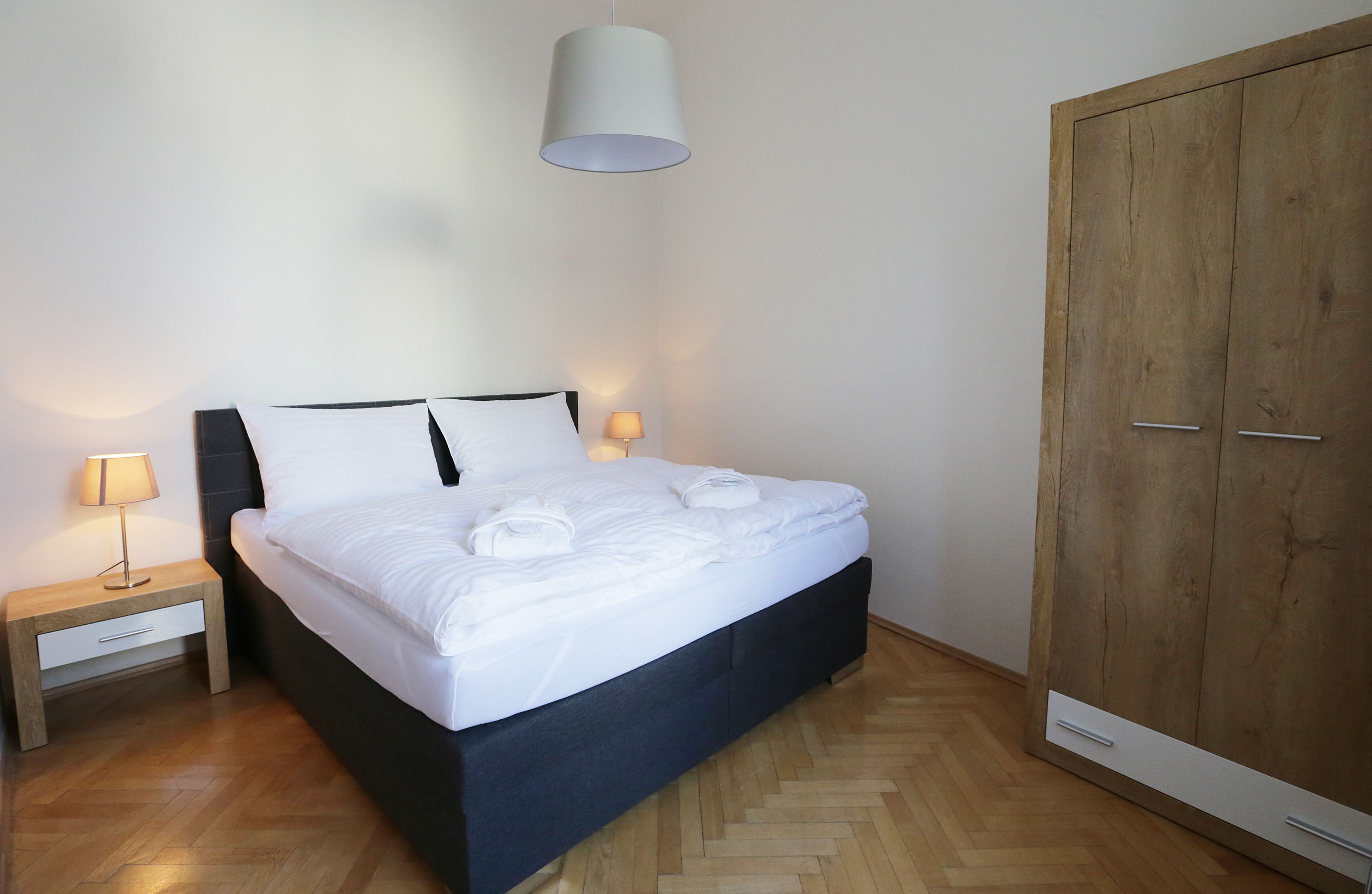 A bedroom with a bed, bedside table, lamp, wardrobe, and a hanging light fixture.