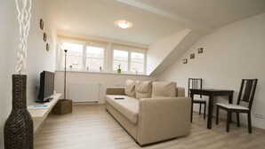 A modern living room with a sofa, a television, a dining table with chairs, and a window with a view of the outside. - Greg Apartments Kampa Prague (Prague)