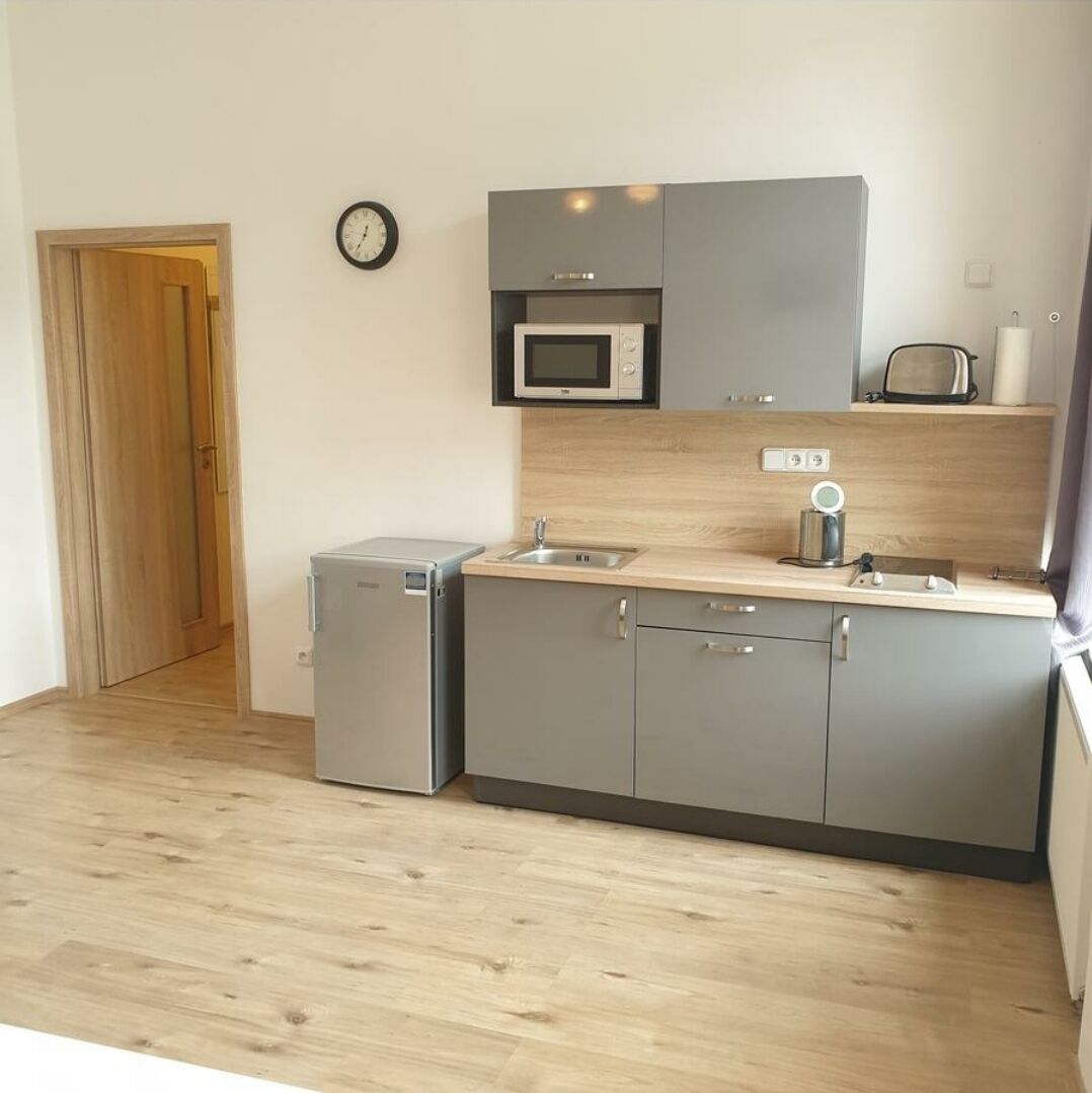 A compact kitchen with grey cabinets, a microwave, a coffee machine, and a small refrigerator.
