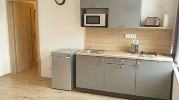 A compact kitchen with grey cabinets, a microwave, a coffee machine, and a small refrigerator.