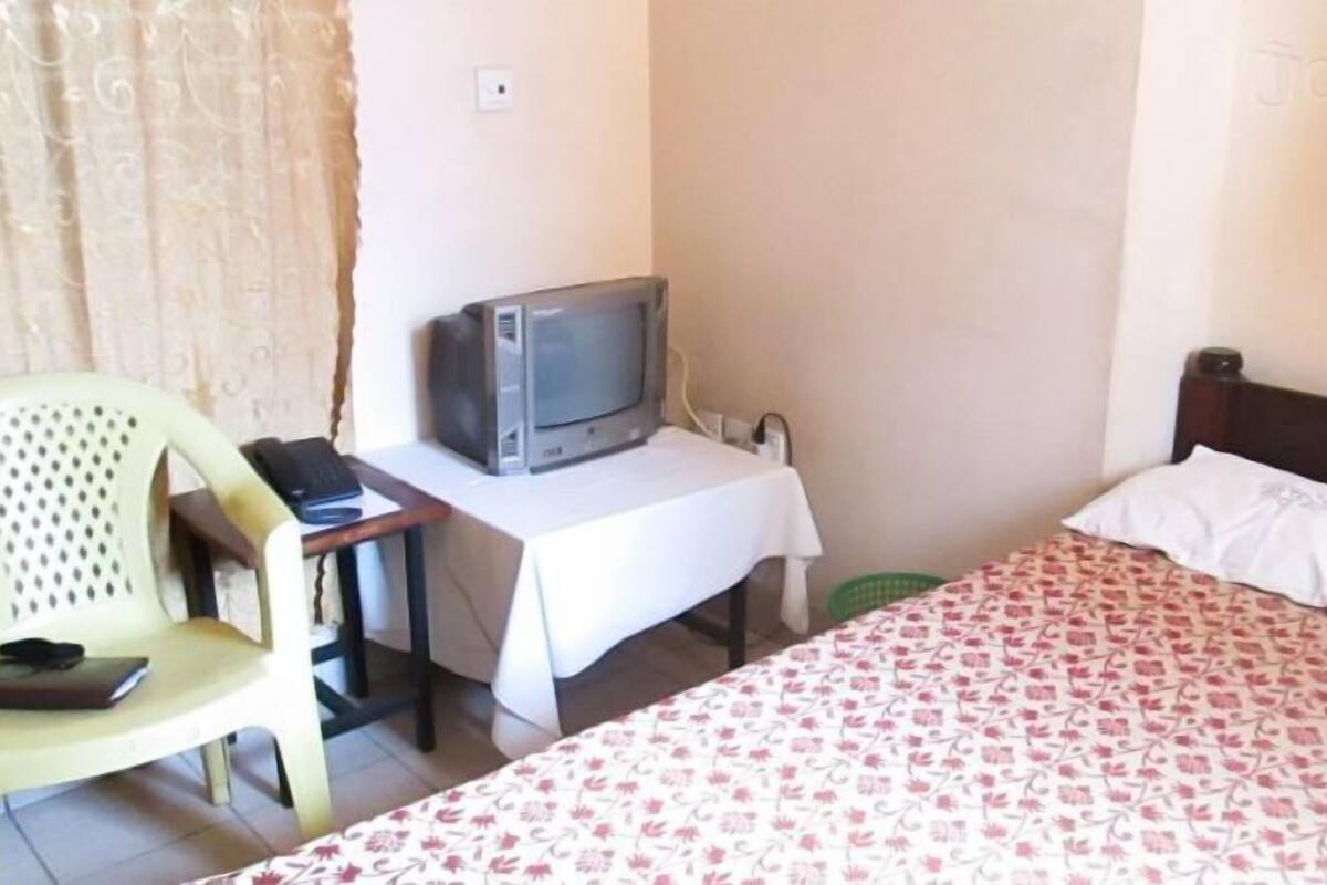Una habitación con una cama, un escritorio con una computadora, una silla y un televisor.
