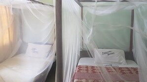 Twee enkele bedden met muskietennet, elk met een kussen en een label met de tekst 'Panorama Gardens Hotel'.