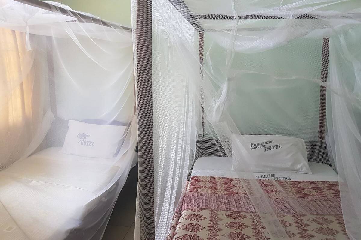 Dos camas individuales con mosquitero, cada una con una almohada y una etiqueta que dice "Panorama Gardens Hotel".