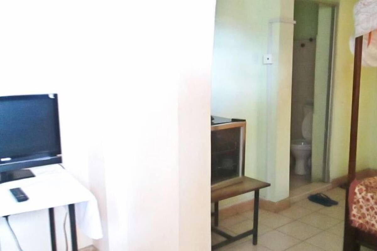 Una habitación con cama, televisión, una mesita y un baño visible a través de una puerta abierta.