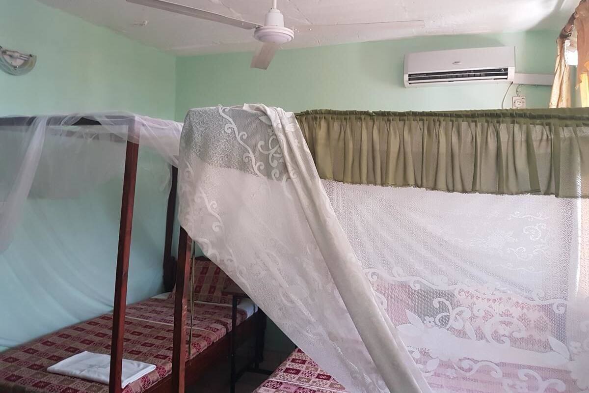 Una habitación con cama, ventilador de techo, aire acondicionado y ventana con cortinas.