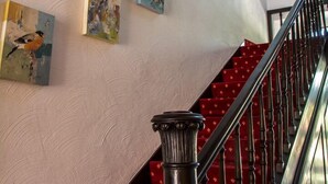 Eine Treppe mit rotem Teppich und schwarzen Geländern, die zu einer Fläche mit einer weißen, strukturierten Wand und mehreren gerahmten Kunstwerken führt.