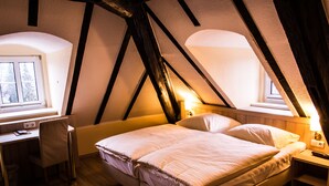 Ein Schlafzimmer mit schrägem Dach, einem Bett, einem Schreibtisch und einem Stuhl.