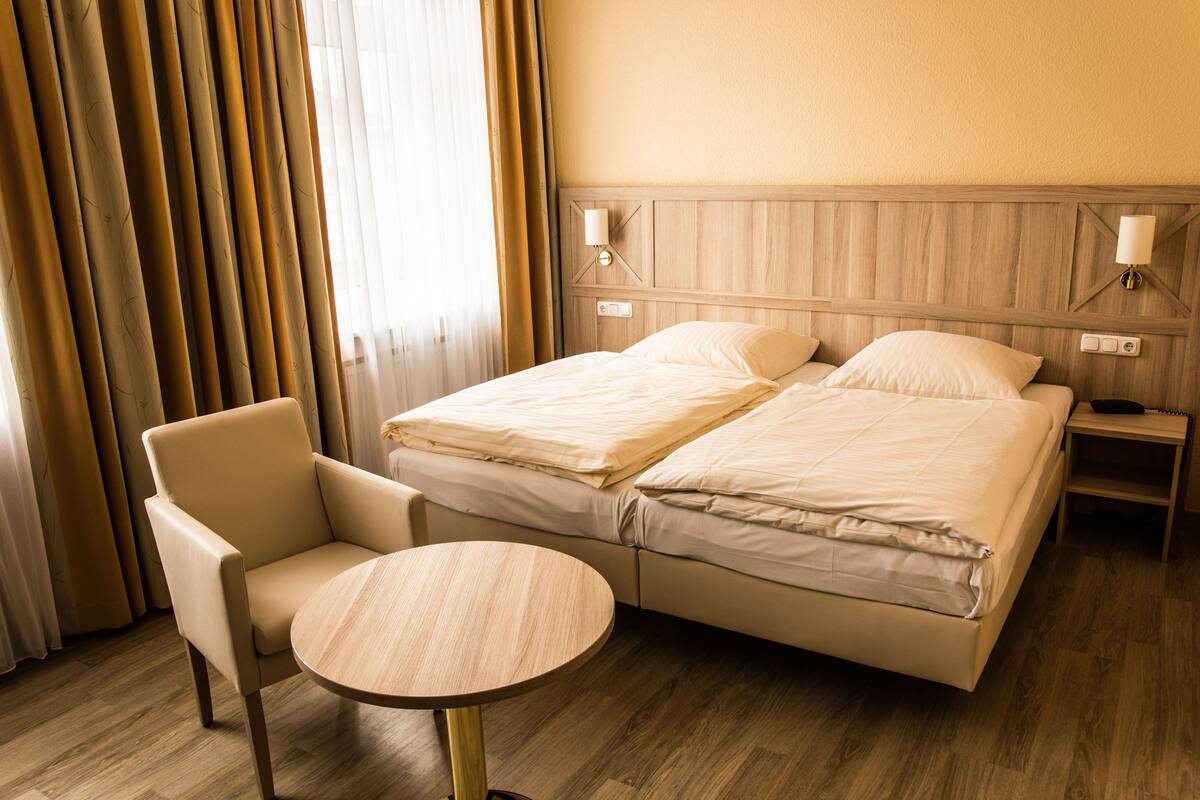 Une chambre d’hôtel avec un lit double, une chaise, une petite table ronde et une table de chevet avec une lampe.