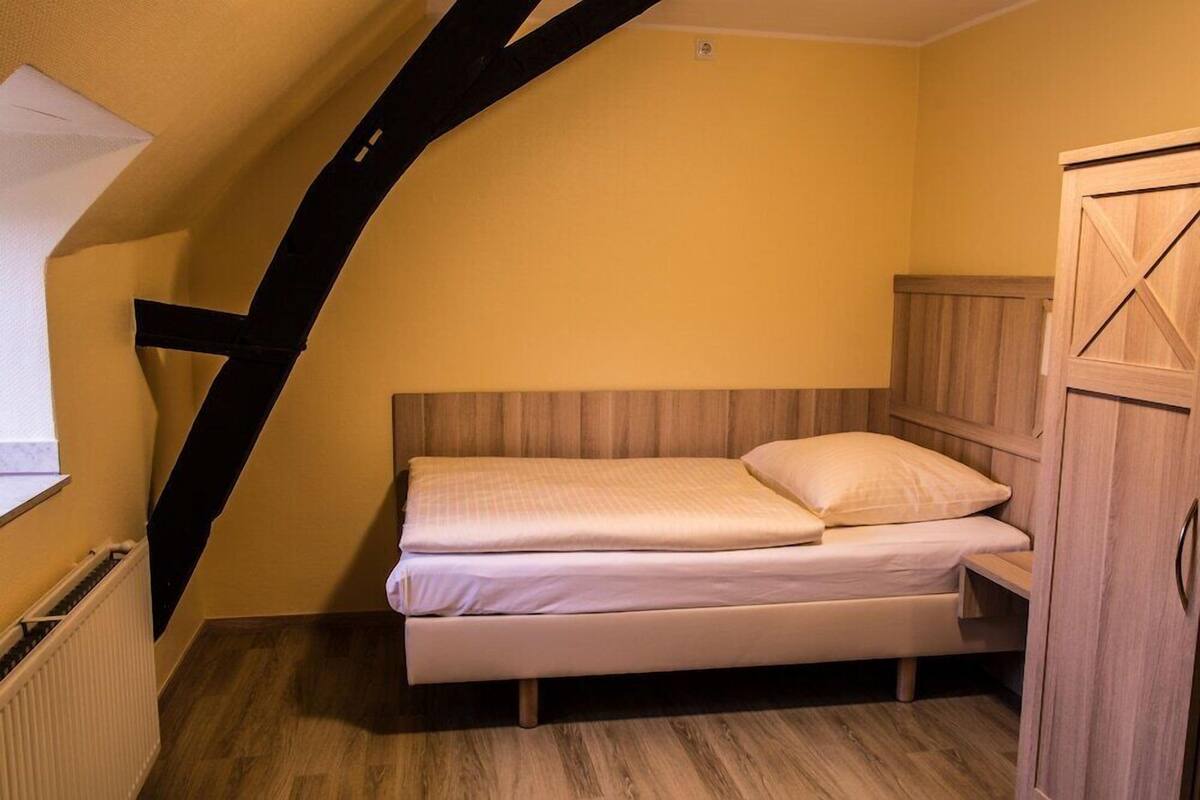 Un lit simple dans une pièce aux murs en bois et au plafond en pente.