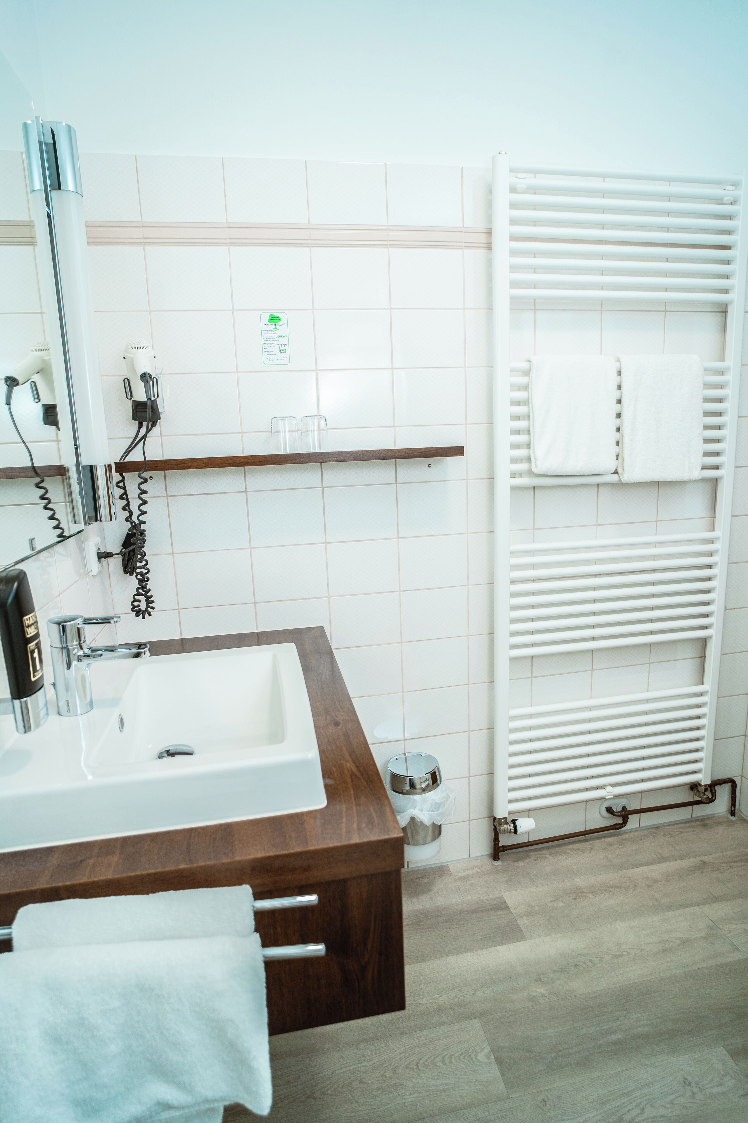 Un baño con tocador de madera, un lavamanos blanco, un perchero para toallas, un radiador blanco y un espejo.