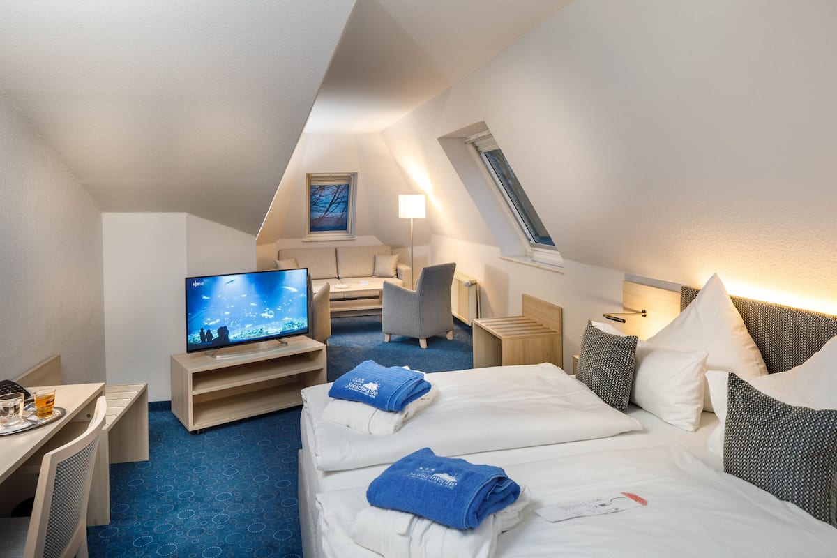 Ein Hotelzimmer mit Fernseher, Schreibtisch, Stuhl, einem Bett mit Handtüchern und einem Fenster.