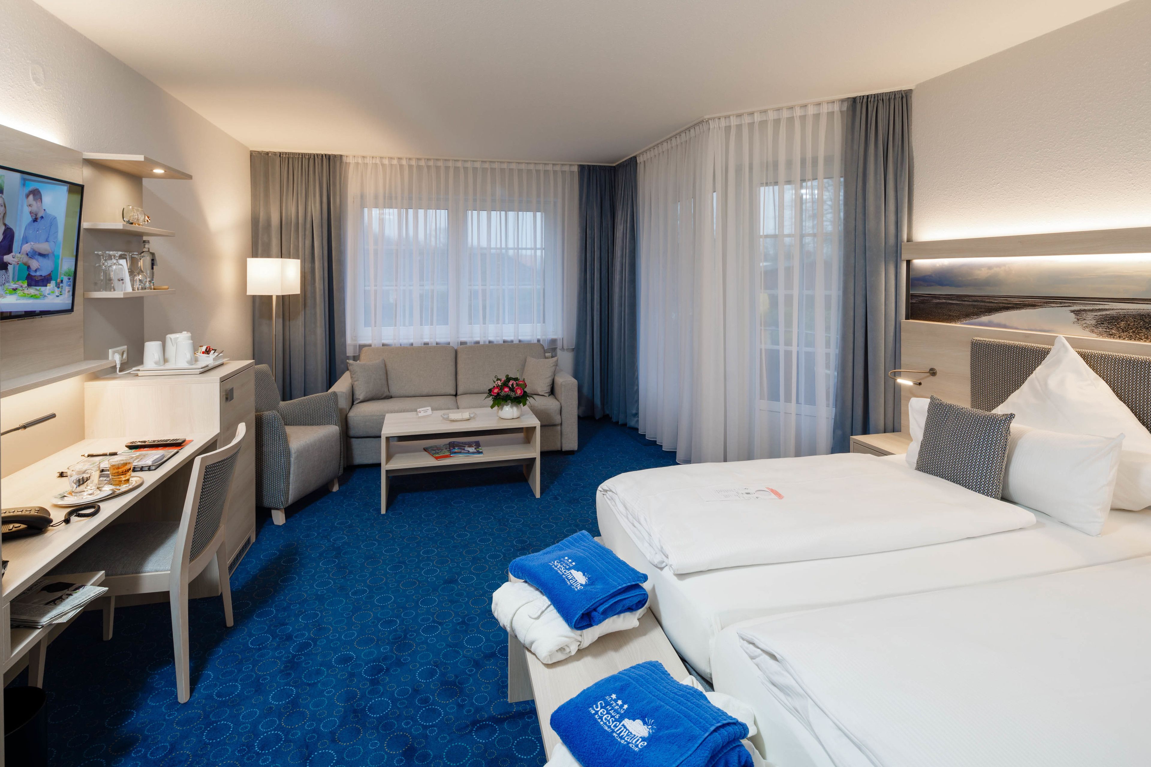 A hotel room with a bed, a desk, a sofa, a TV, and a window with curtains.