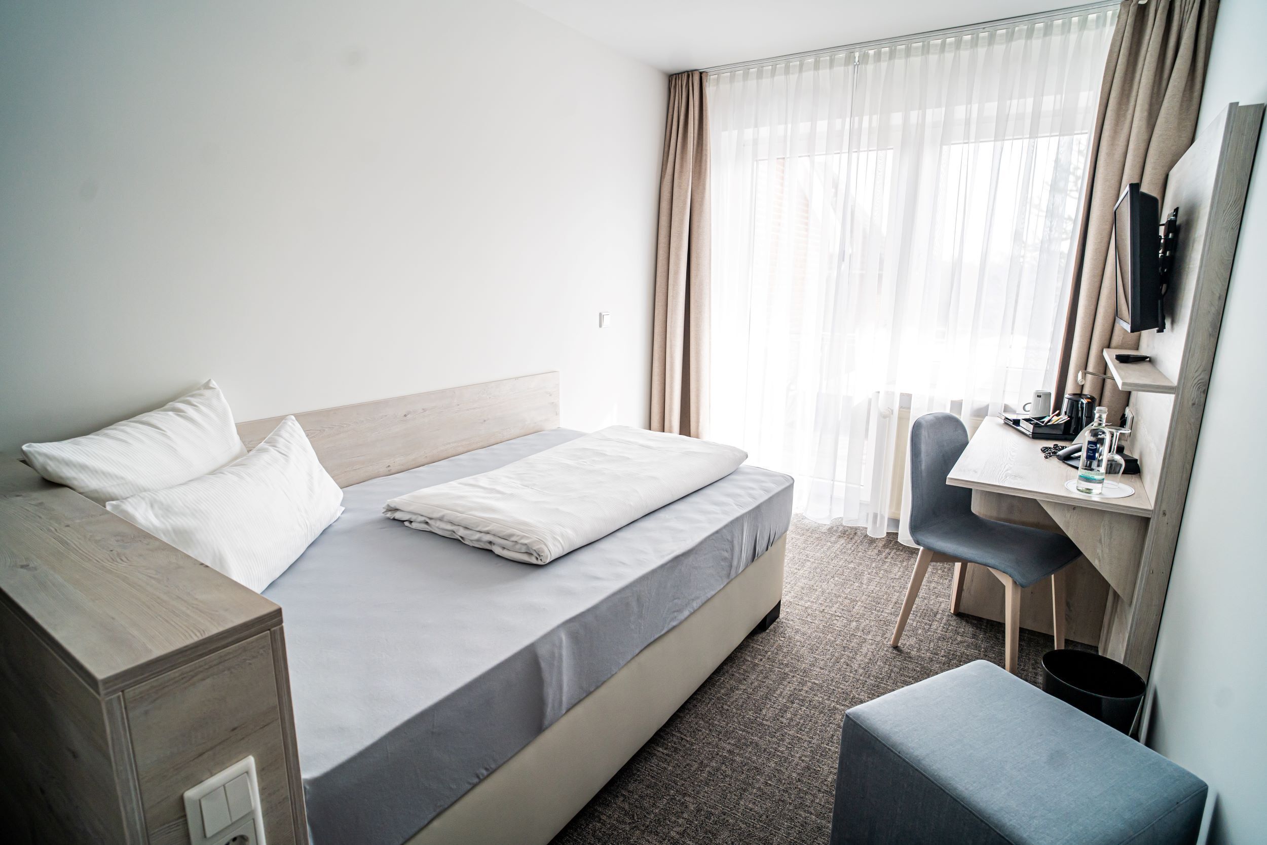 A hotel room with a bed, a desk, a chair, and a television.