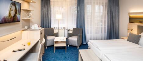 Una habitación de hotel con cama, escritorio, silla, televisor y una mesita.