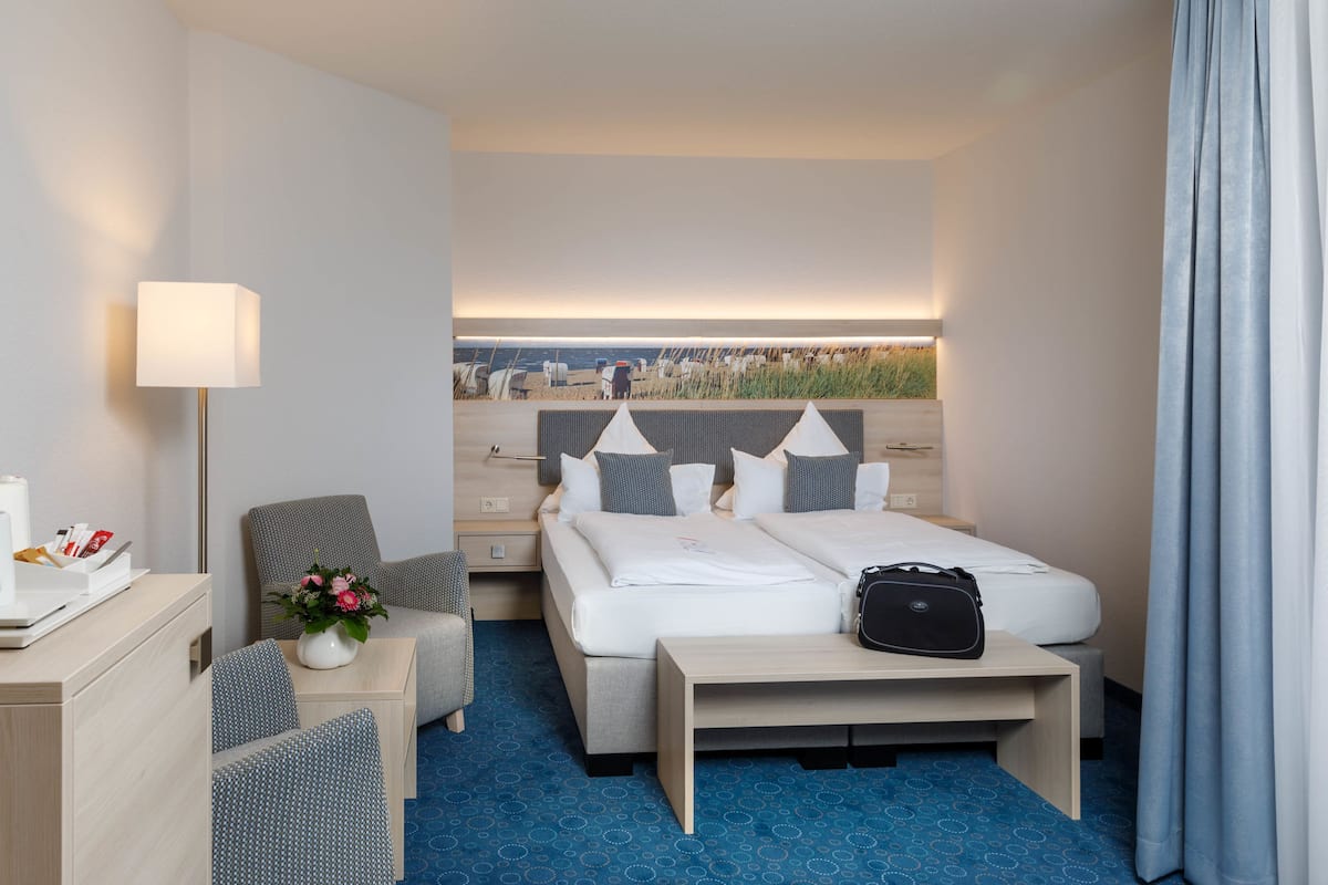 Ein Hotelzimmer mit Bett, Nachttisch, Lampe und Blick auf den Strand.