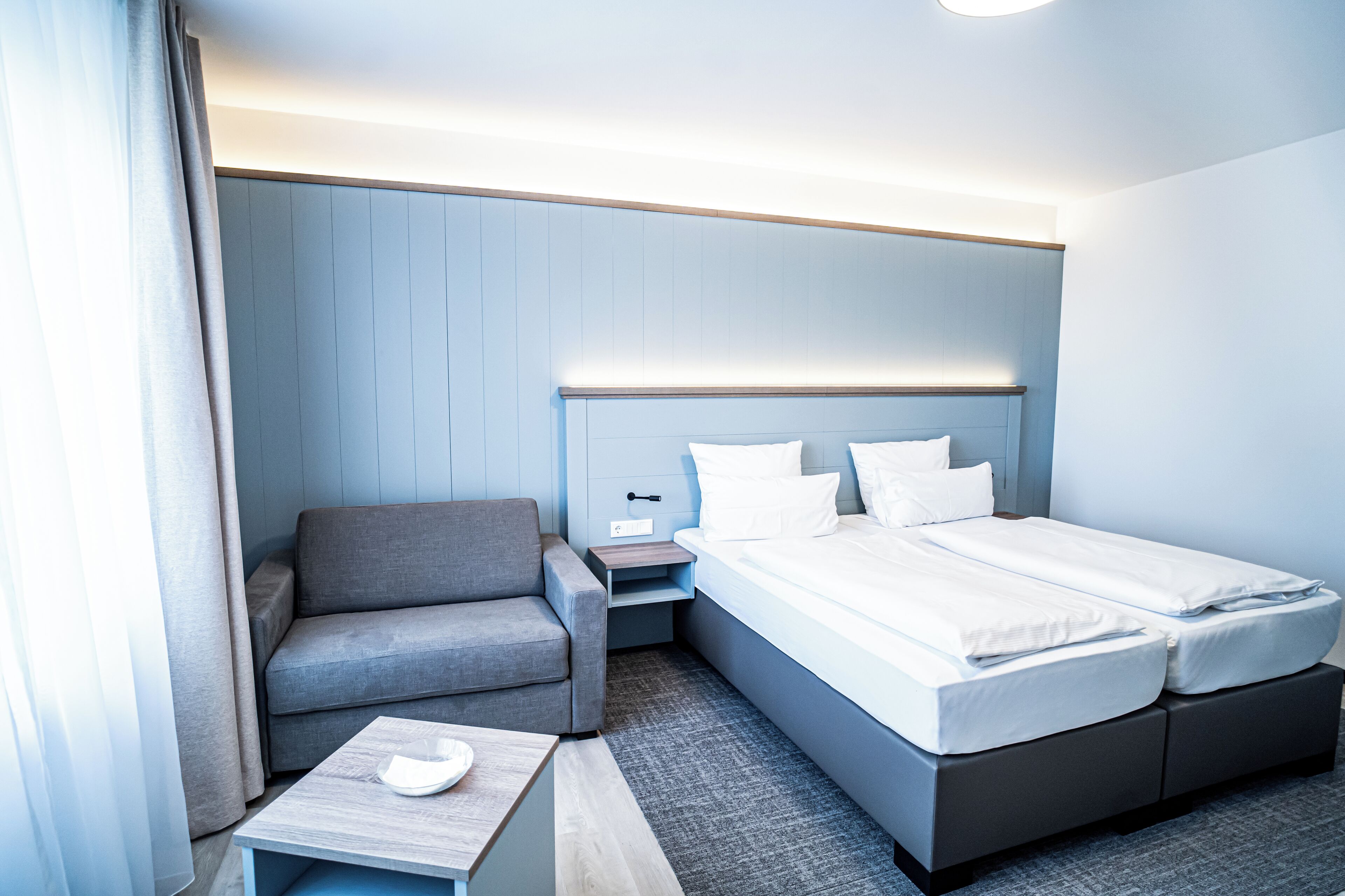 Una habitación de hotel con una cama, un sofá, una mesita de noche y una pequeña mesa.