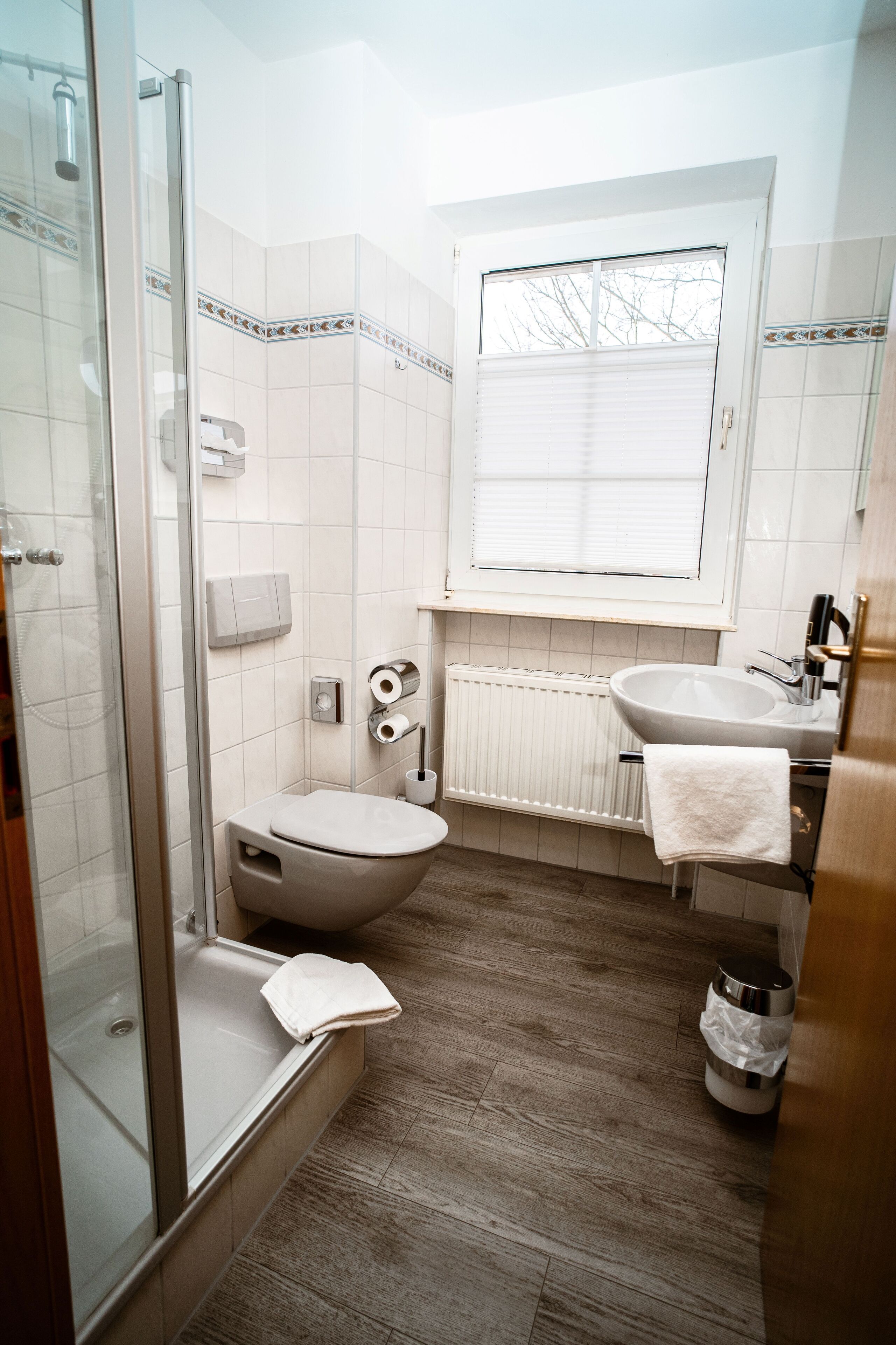 A bathroom with a glass shower enclosure, a toilet, a sink, and a window.