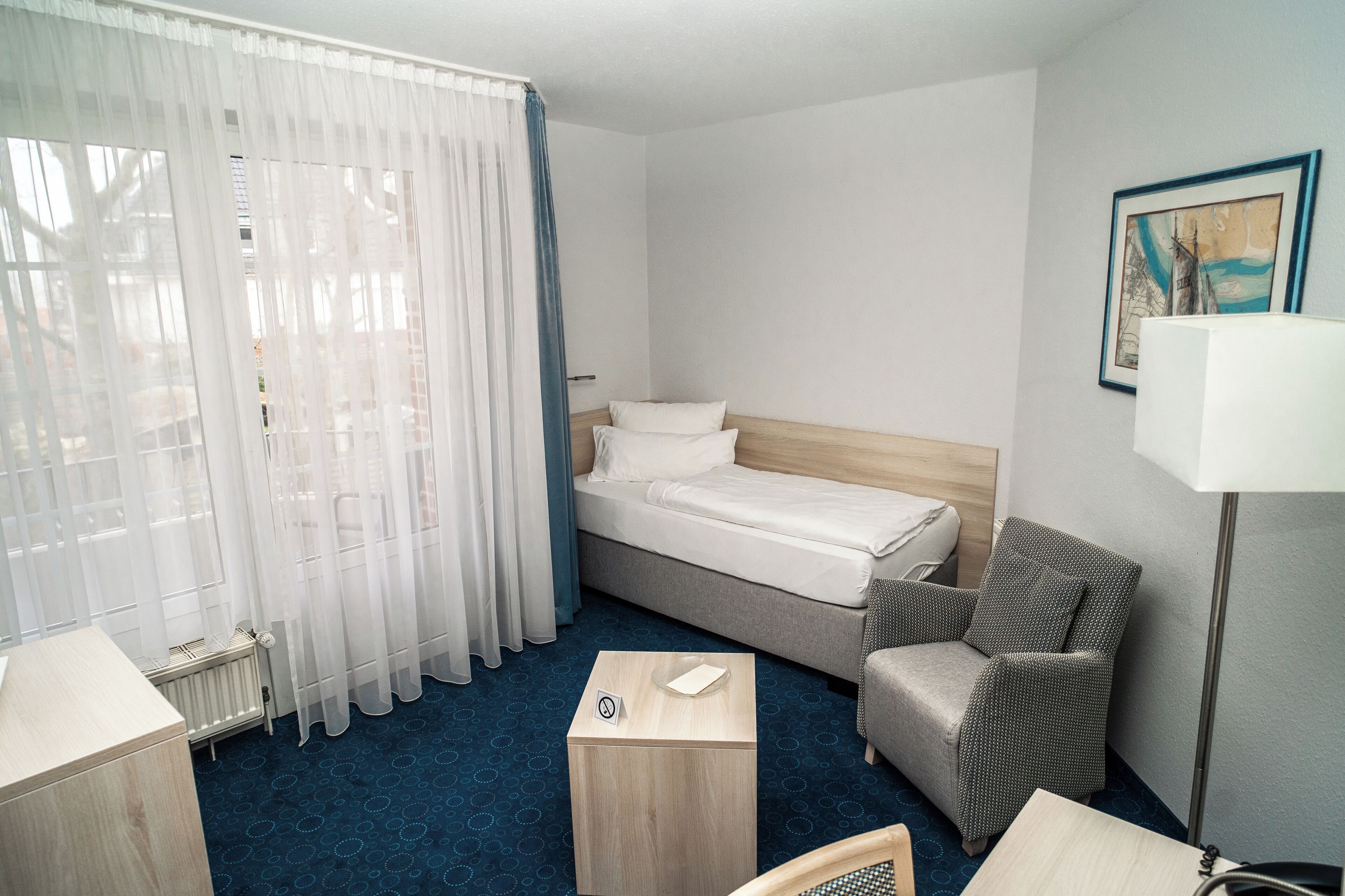 A hotel room with a bed, a chair, a table, and a lamp.
