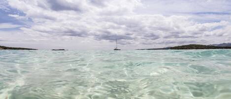 A clear view of a body of water with a sailboat in the distance and a mountainous landscape on the horizon.