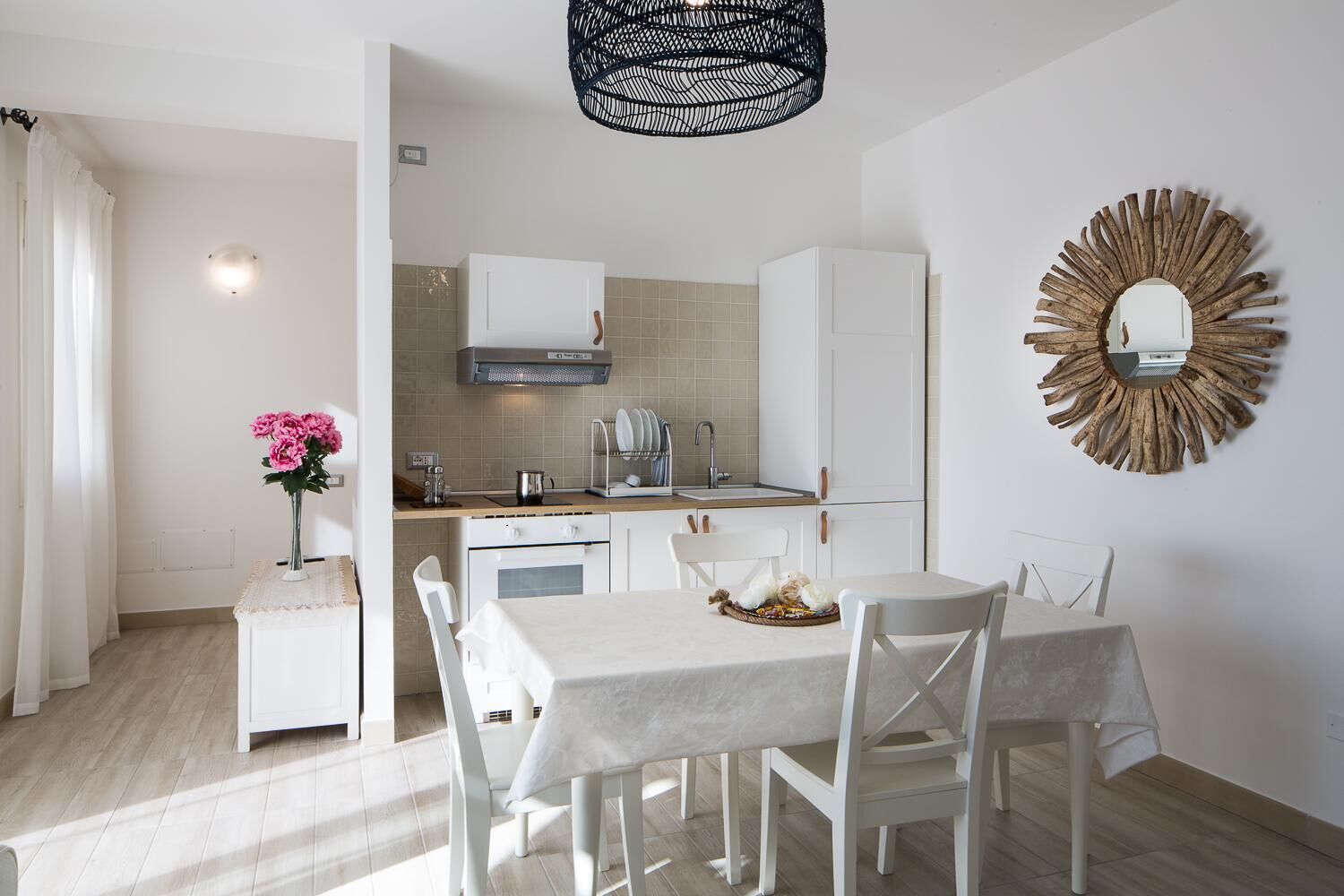 A modern kitchen with white cabinets, a built-in oven, and a dining area with a table and chairs.