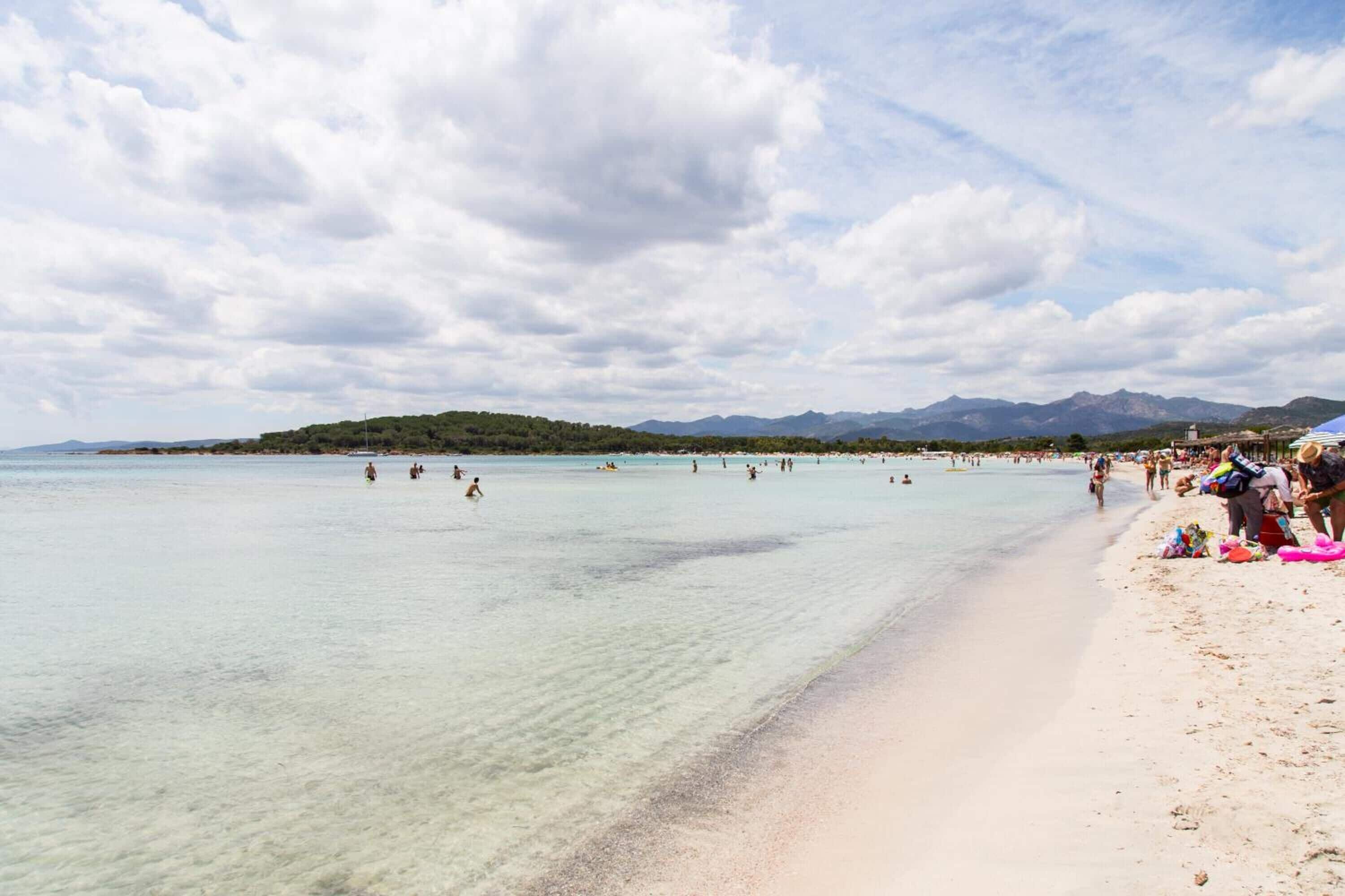 A beach with clear water, a sandy shore, and mountains in the background.