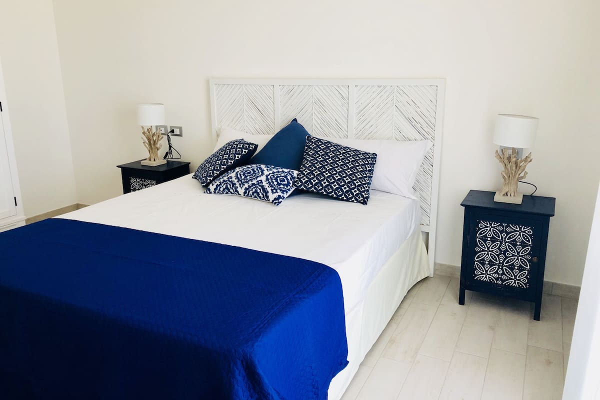 A neatly made bed with a white headboard and blue bedding, flanked by two nightstands with decorative lamps.