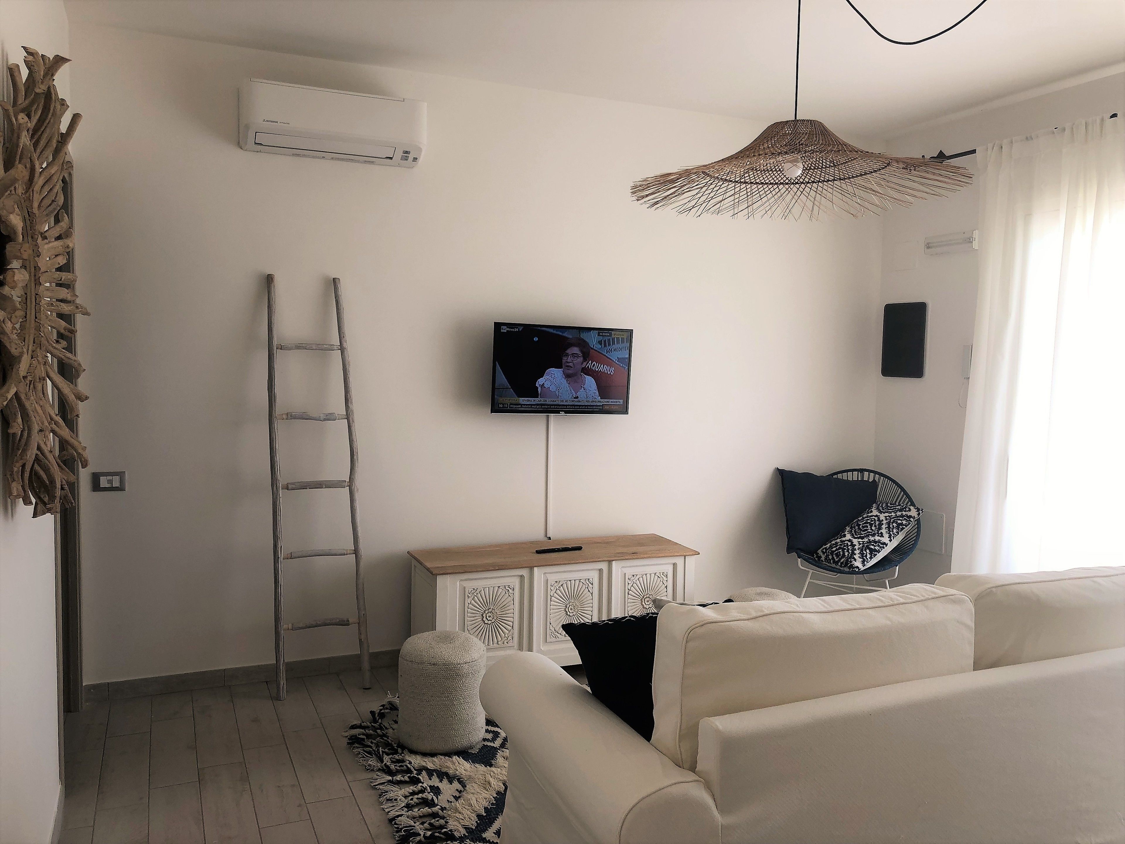 A living room with a white sofa, a television mounted on the wall, a woven pendant light, and a ladder against the wall.