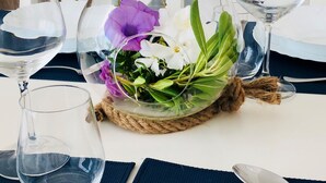 Une table à manger ornée d’un centre de table composé d’un vase en verre contenant des fleurs et des feuilles, entourée de verres à vin et de couverts.