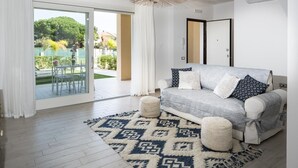Un salon moderne avec un canapé gris, un tapis à motifs et une vue sur un jardin, visible à travers des portes vitrées.