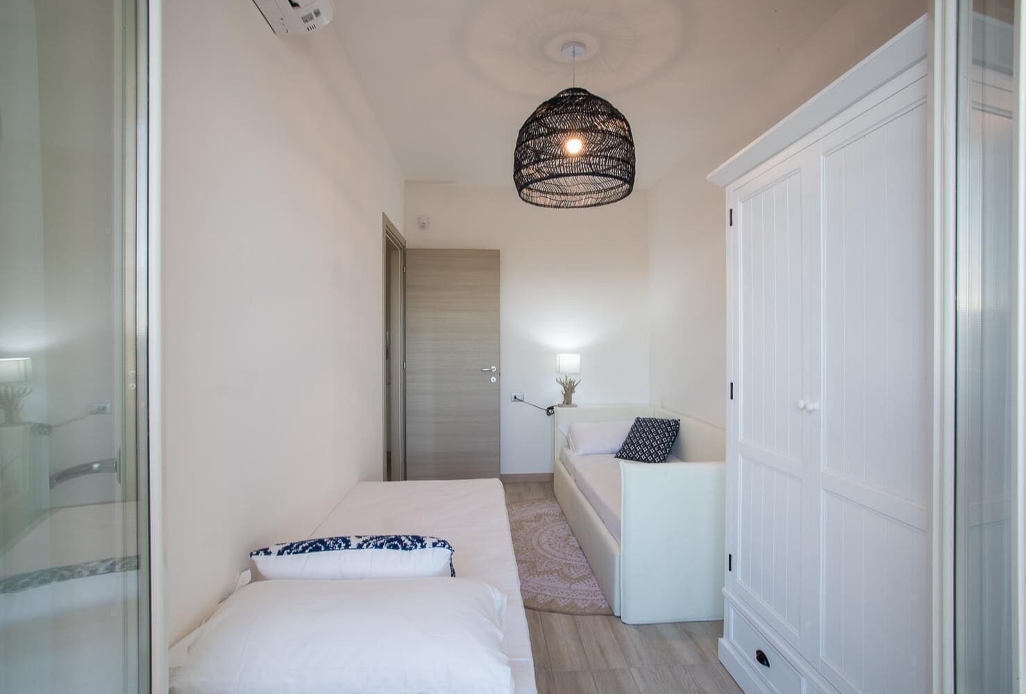 A bedroom with a bed, a nightstand, a wardrobe, and a hanging light fixture.