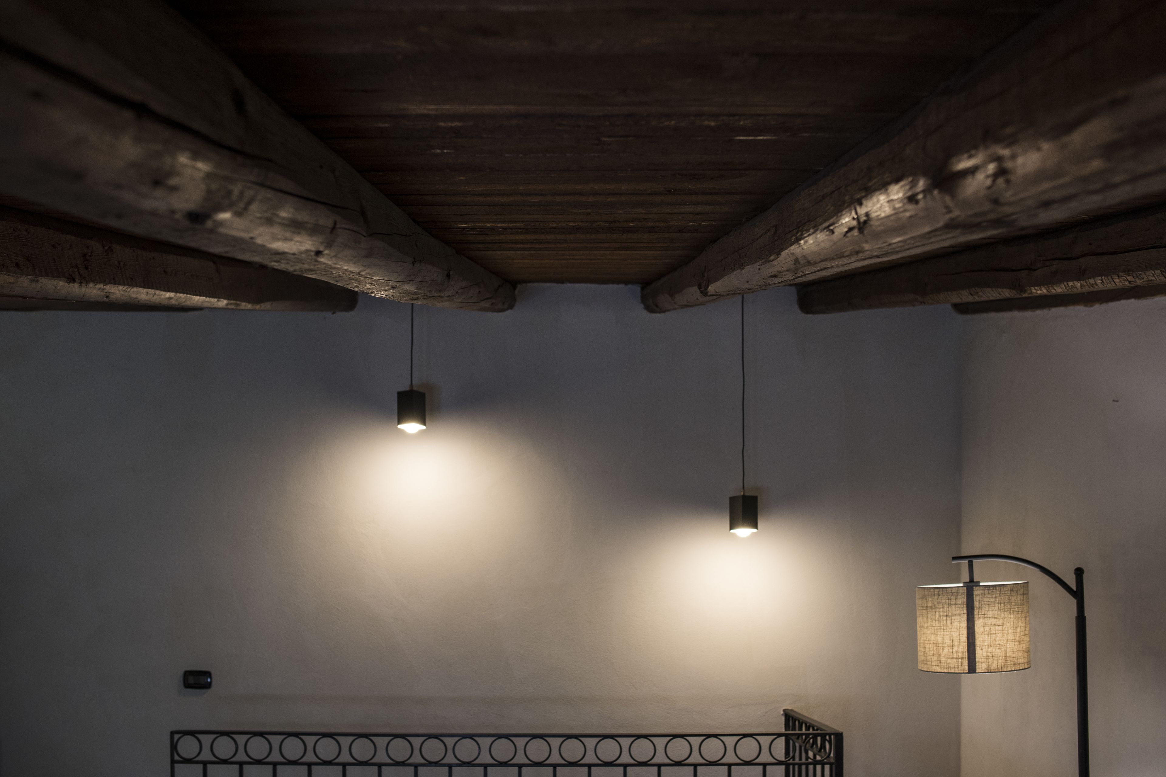 A room with exposed wooden beams, a metal bed frame, and two pendant lights.