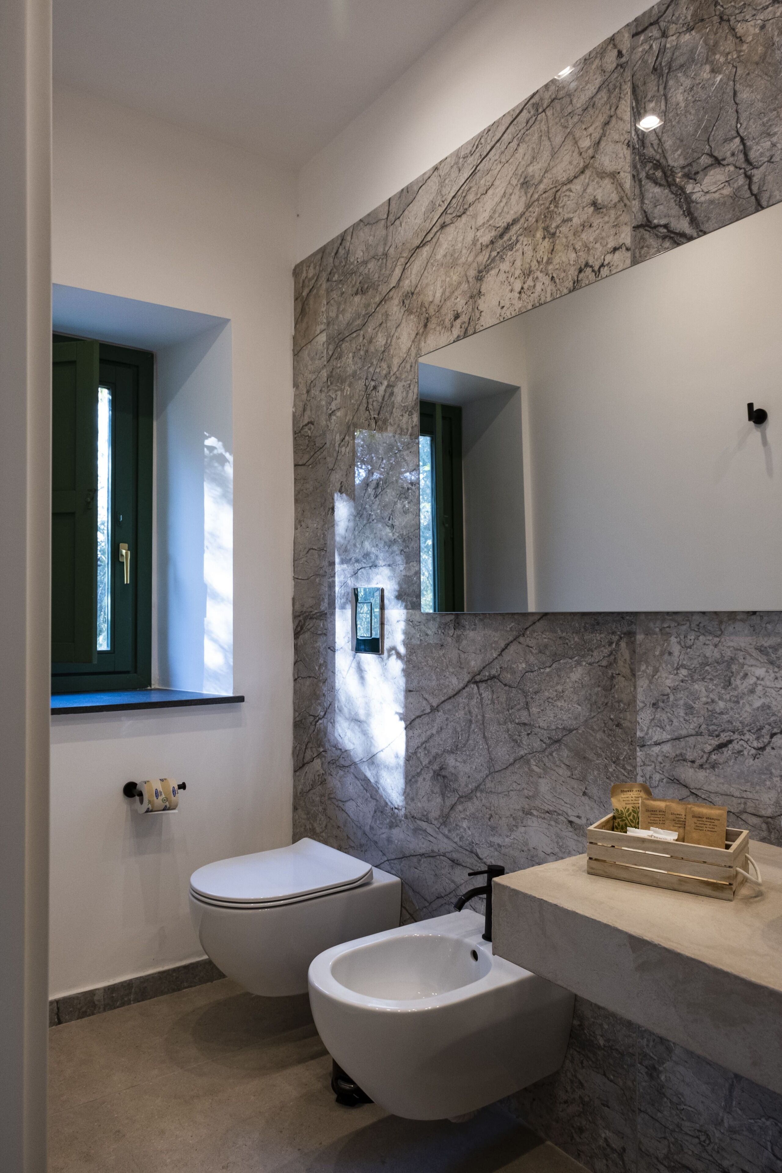 A modern bathroom with a toilet, bidet, and a marble backsplash.