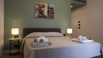 A neatly made bed with folded towels, a wall-mounted painting, and a bedside lamp.