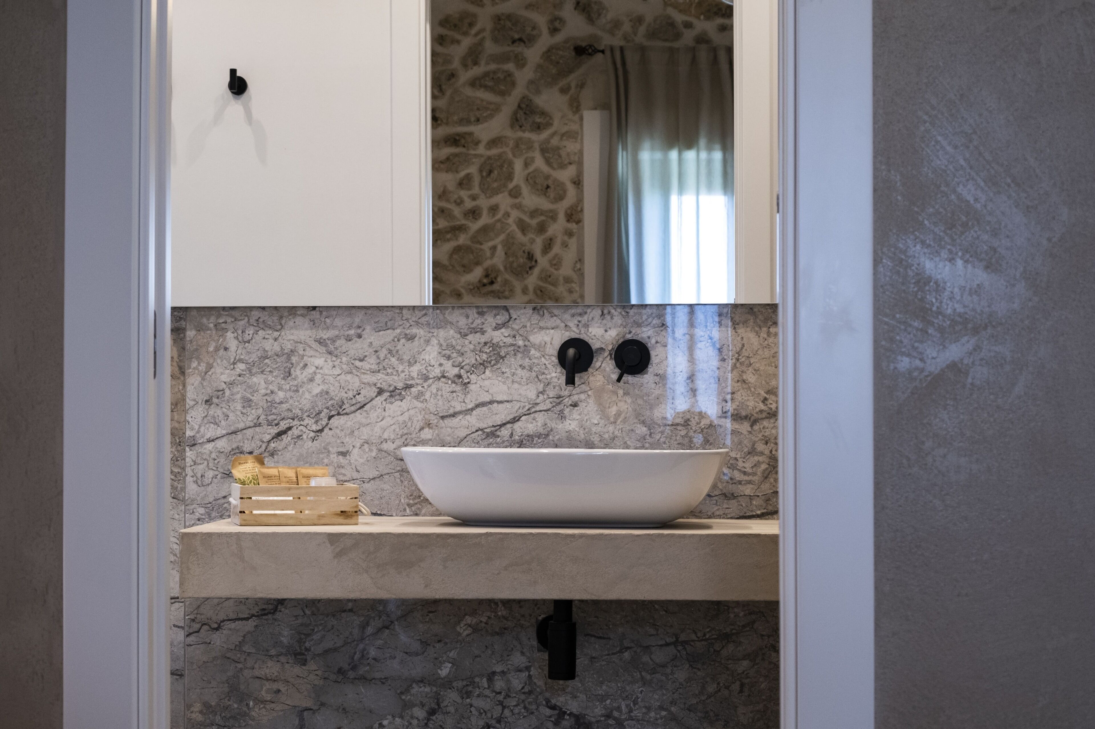 A bathroom with a white vessel sink, marble backsplash, and a stone wall.