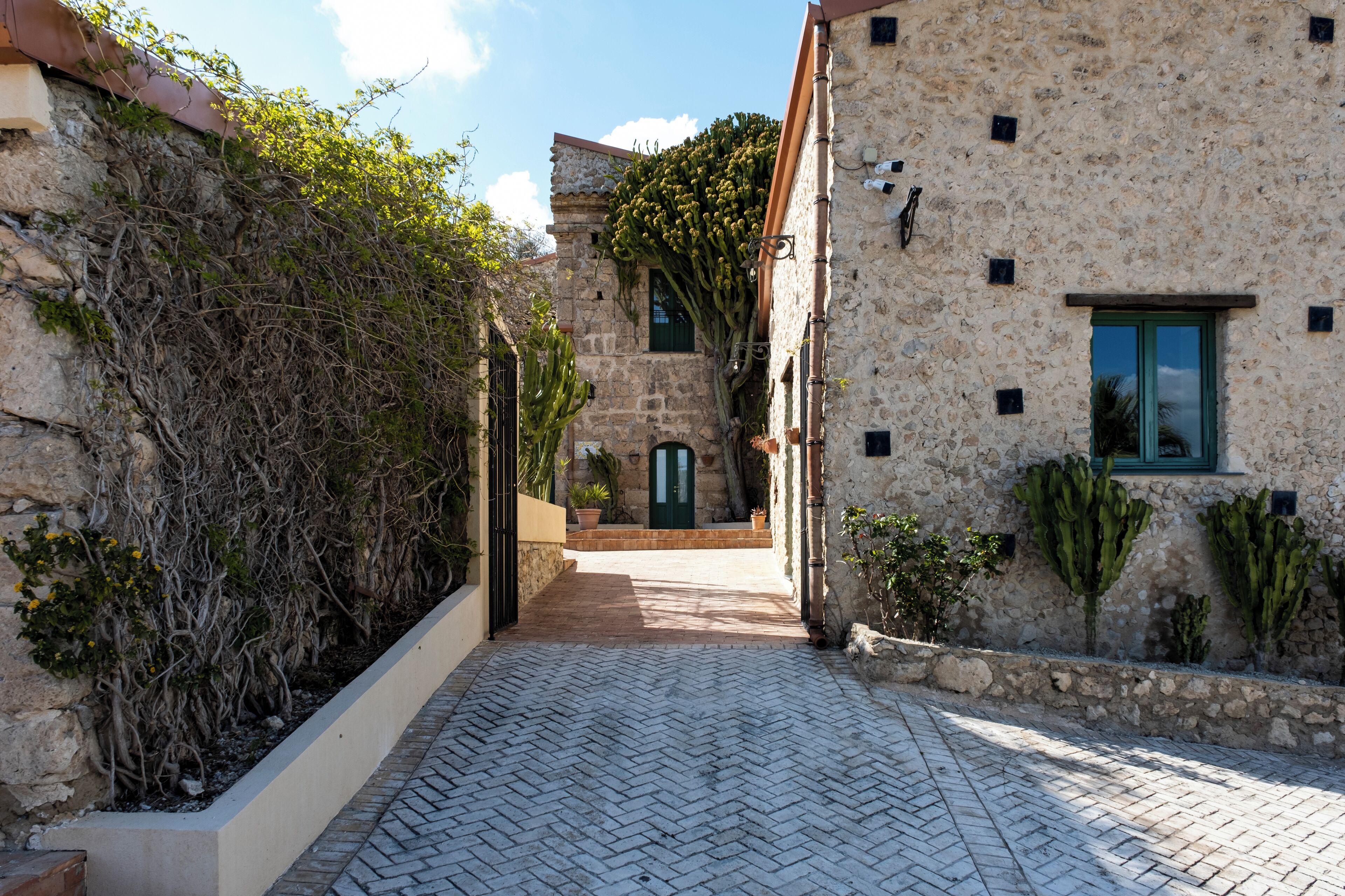 A narrow stone pathway leading to a building with a green door and a window.