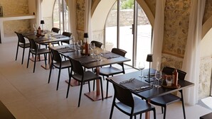 Un comedor con varias mesas y sillas, amplias ventanas de arco y paredes de piedra.