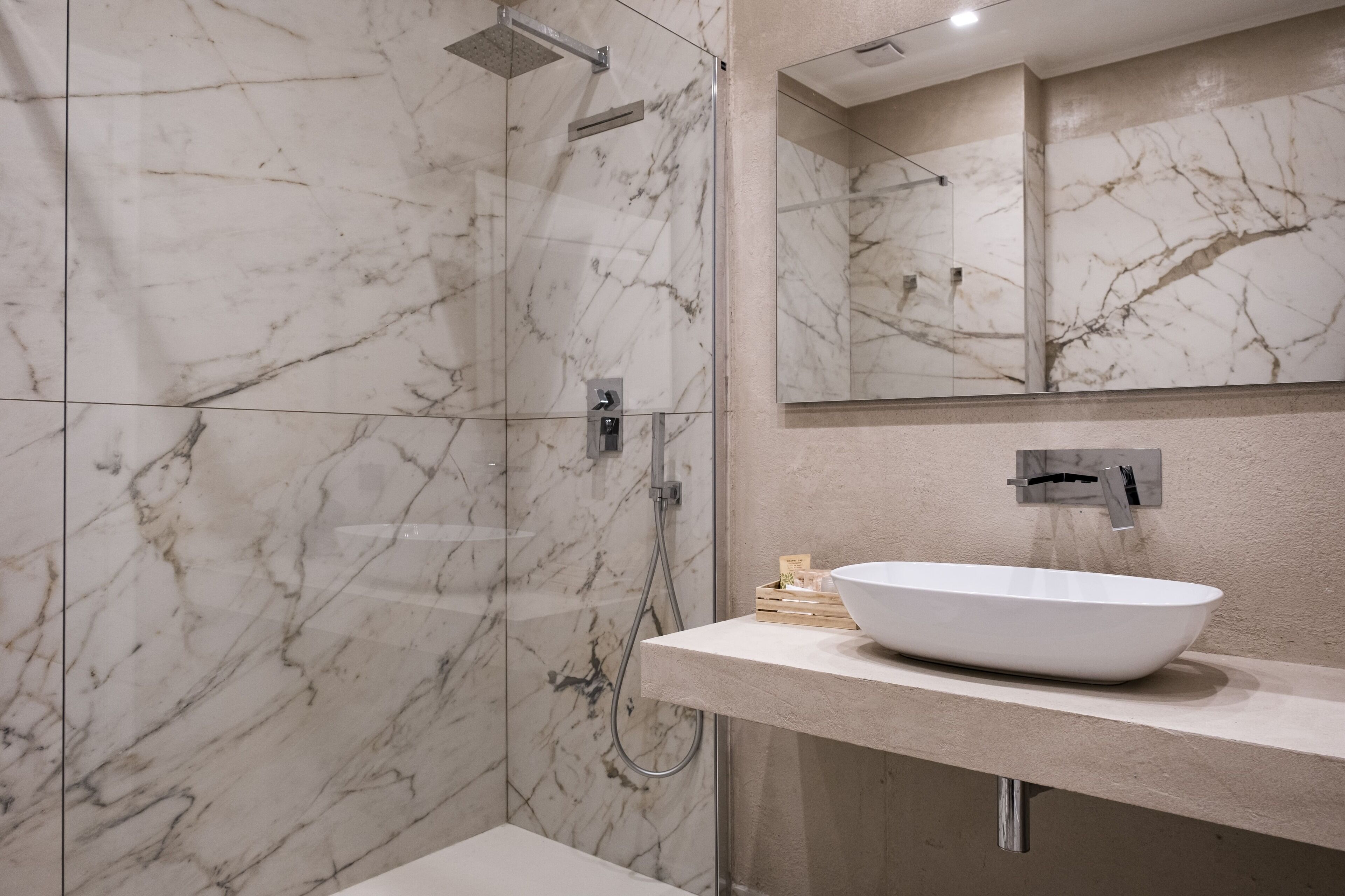 Een moderne badkamer met een douchewand van marmer, een witte wastafel en een grote spiegel.