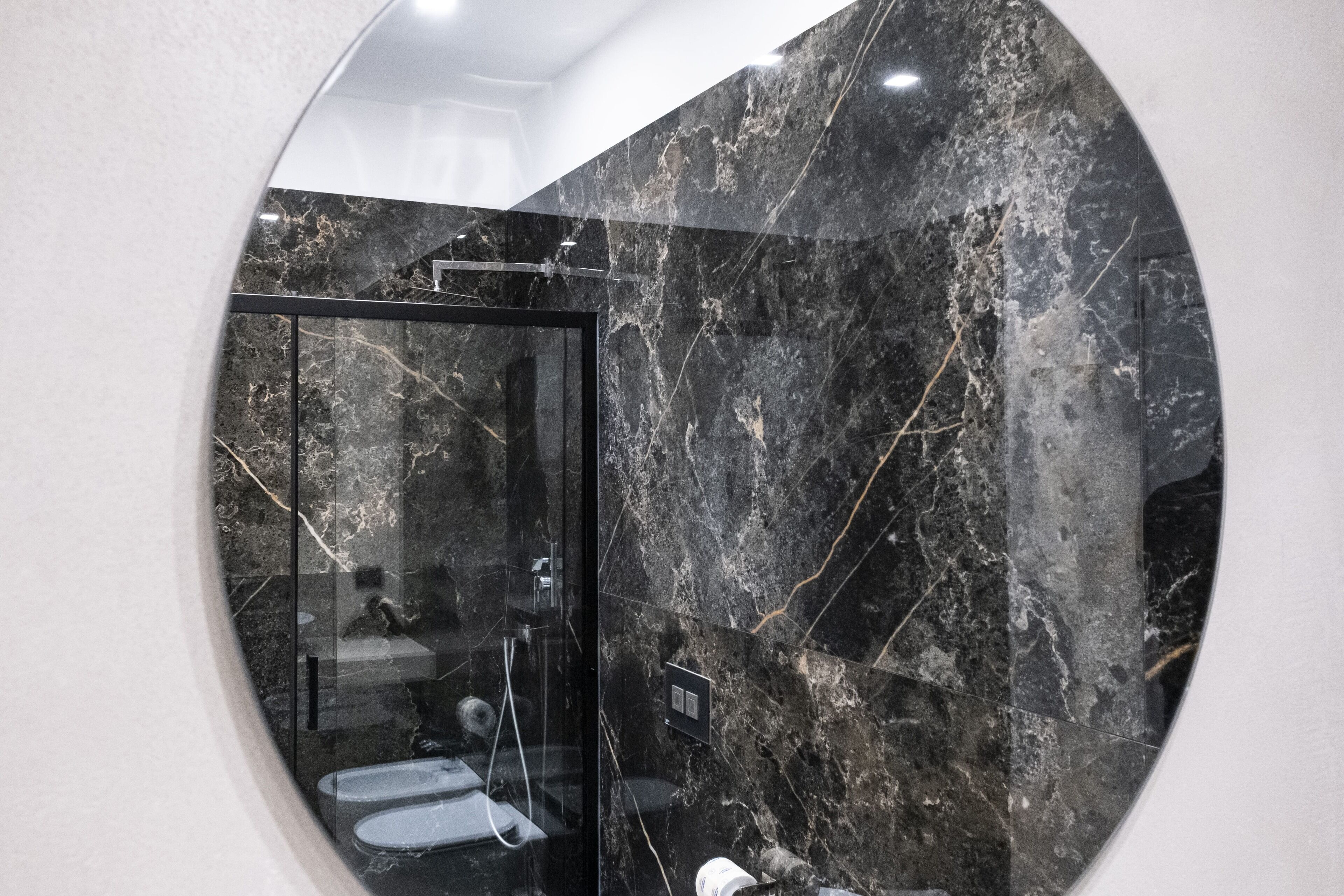A modern bathroom with a glass-enclosed shower, marble walls, and a visible toilet.